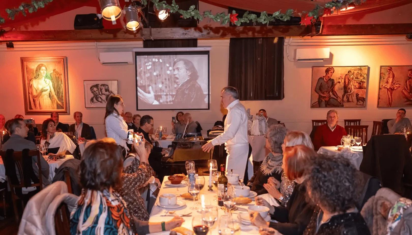 Comedor de La Castafiore con los cantantes actuando entre las mesas y los cuadros de Camilo Porta en la pared