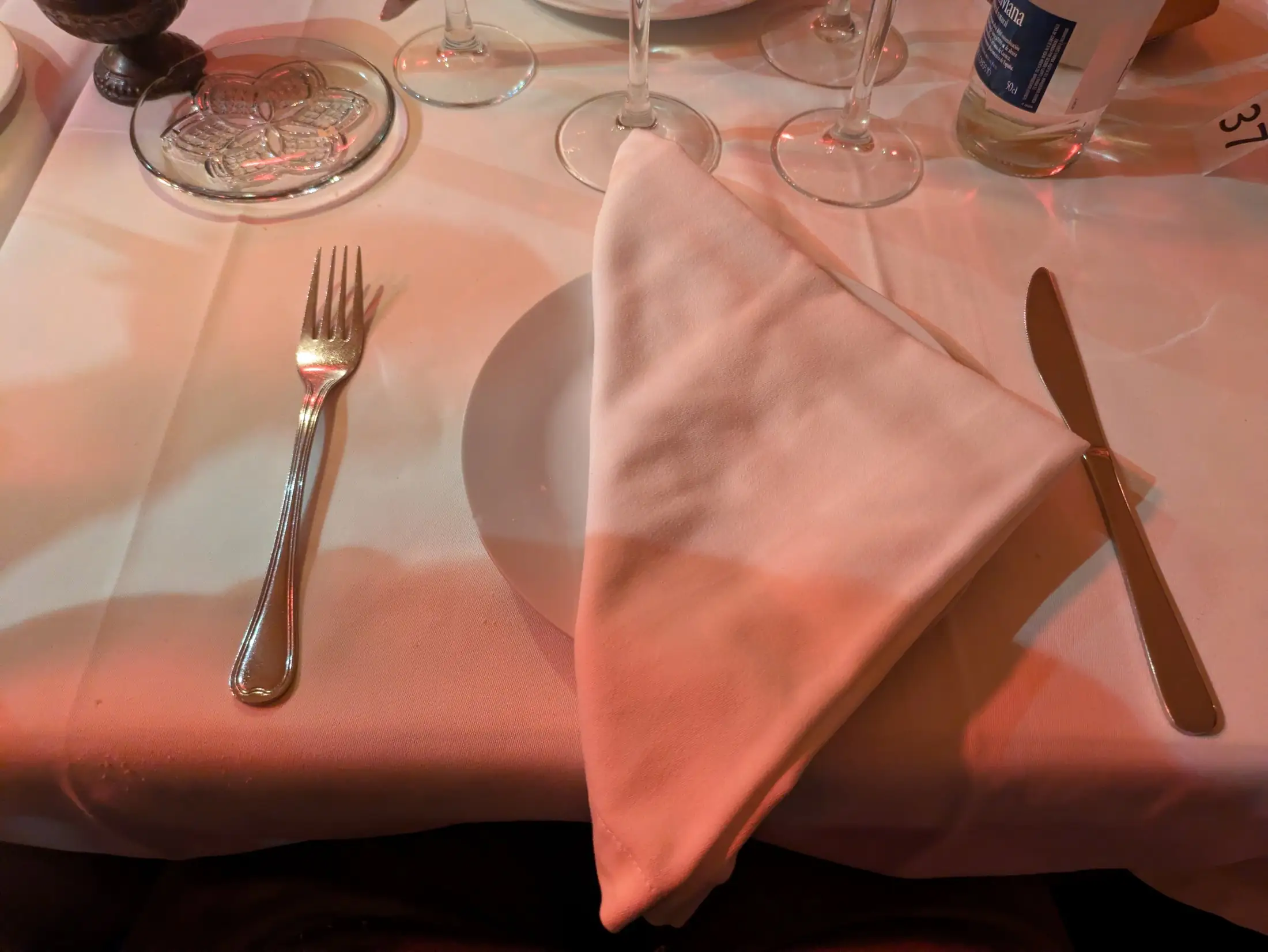 Mesa preparada en La Castafiore con mantel blanco, copas y la luz rosada de la sala
