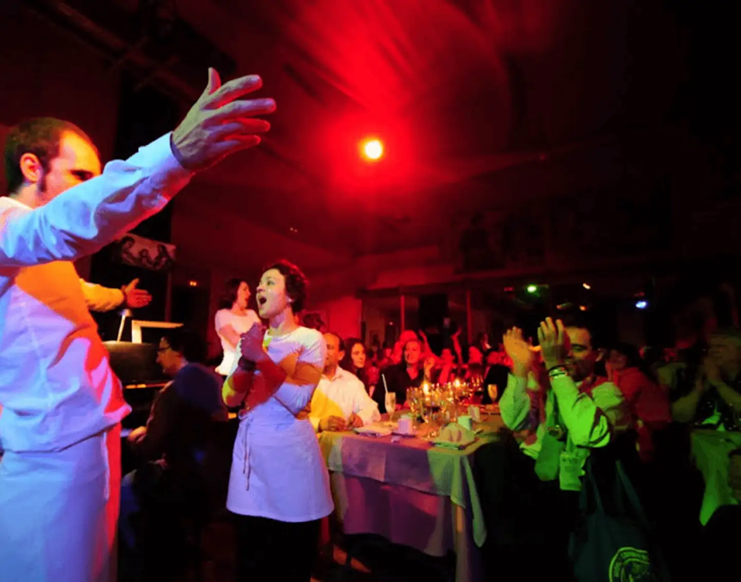 Cantantes con delantal blanco actuando entre las mesas mientras los comensales aplauden